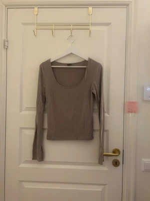 Beige långärmad topp med rund hals - Snygg beige långärmad topp med djup rundad halsringning. Toppens material känns mjukt och stretchigt, perfekt för en clean och stilren look. Passformen är slim och ärmarna är extra långa för en trendig vibe.