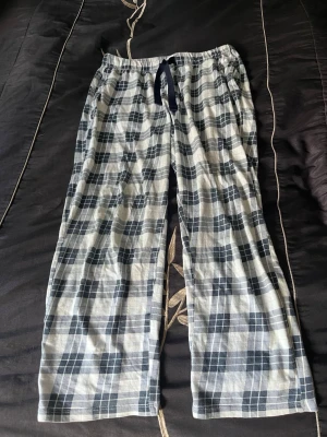 Rutiga pyjamasbyxor - Mysiga pyjamasbyxor i vitt och mörkblått rutmönster. Byxorna har ett mörkblå snöre för justerbar passform. Tillverkade i mjukt och lätt tyg, perfekta för chillkvällar hemma. Använt några gånger tills dom råkade bli torktumlade så dom blev för kort så skulle säga att dom blev en storlek mindre.