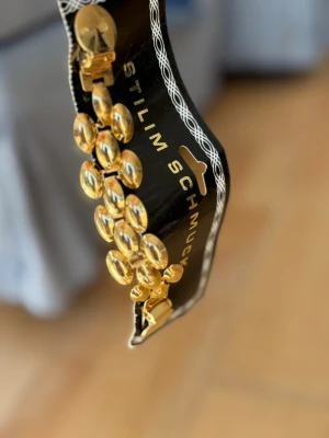 Guldfärgat dekorativt smycke  - Snyggt dekorativt smycke som kan fästas på kläder, accessoarer, skor från Stilim Schmuck i guldfärgad metall med ovala länkar som ger en cool och trendig look. Perfekt accessoar för att lyfta din outfit med lite extra bling. Den har en klassisk design med blanka, rundade detaljer.