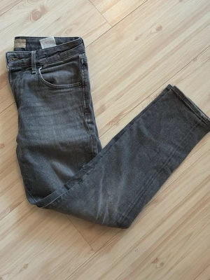 Grå raka jeans med fem fickor - Säljer ett par grå jeans med klassisk femficksmodell och raka ben. Jeansen har bälteshällor och knappgylf. Perfekta för en avslappnad och stilren look. Materialet är denim i bomull. Snygga att matcha med sneakers eller boots.