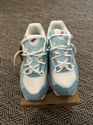 Asics blåvita sneakers mesh & skinn - Snygga sneakers från Asics i ljusblått och vitt. Ovandelen är i mesh och skinn för en sportig look och bra andningsförmåga. Klassisk låg modell med vita snören och detaljerad sula. Perfekta för dig som gillar stilrena och bekväma skor.