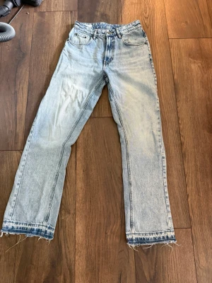 Ljusblå flared jeans med rå kant - Säljer ett par ljusblå jeans med flared passform och råa, fransiga benslut. Klassisk femficksmodell i denim med hög midja och dragkedja. Perfekta för en avslappnad och trendig look.