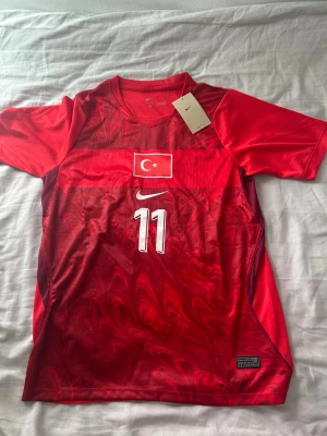 Turkiet matchtröja Nike röd #11 - Säljer en officiell Turkiet matchtröja från Nike i rött med vita detaljer och nummer 11. Tröjan har Turkiets flagga på bröstet, YILDIZ och siffran 11 på ryggen samt korta ärmar. Tillverkad i lätt och ventilerande funktionsmaterial, perfekt för fotboll. Storleken är S men sitter lite mer som en M