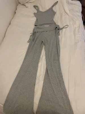 Grått ribbat set med utsvängda ben - Lounge set Snyggt tvådelat set i ljusgrått ribbat material. Setet består av ett linne med smala axelband och matchande byxor med utsvängda ben och knytband på sidan för design. Perfekt för dig som gillar en trendig och bekväm stil. På byxorna är det onsynliga fläckar då man inte ser för att tyget är redan lite ”pixligt” därmed drar jag ner priset extra från det originella priset:) otroligt snyggt på! Om man vill se lite effortless men elegant, soft.