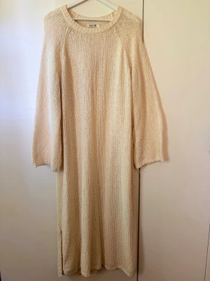 Beige/Vit stickad långklänning Indiska - Beige/Naturvit stickad långklänning från Indiska med rund halsringning, långa vida ärmar & slits längst ner på båda sidor. Klänningen har en relaxed och loose passform, perfekt för dig som gillar en enkel och mysig stil. Klänningen är lite genomskinlig, materialet är grovstickat och ger en avslappnad känsla. Köptes för ca 1 år sedan. Bara använd en gång. Nypris 799kr. 