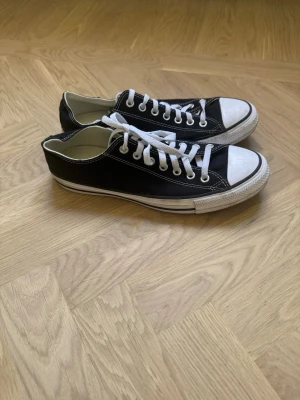 Svarta Converse sneakers med snörning - Klassiska svarta Converse sneakers med vit tå och sula. Skorna har vit snörning och lågt skaft, samt tydliga kontrastsömmar. Perfekta för en avslappnad och cool stil. Materialet är canvas och detaljerna är i gummi.