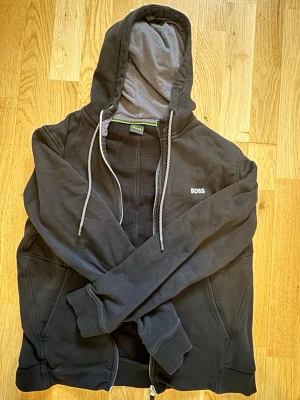 Svart hoodie från BOSS med dragkedja - Hoddie från BOSS. Använt en del men inga skador eller slitage. Tvättas och stryks vid köp och den är i storlek M men kan även passa S..