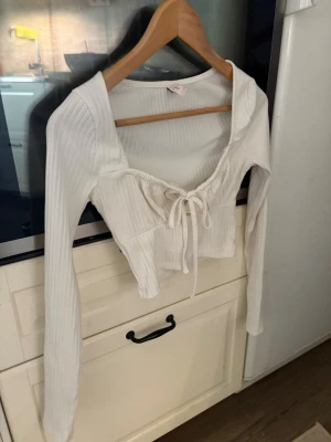 Vit ribbad croppad topp med knyt - Trendig vit långärmad topp med ribbad struktur och croppad passform. Toppen har en snygg knytning framtill och en djupare urringning. Perfekt för dig som gillar stilrena och moderna plagg. Storlek xxs. Säljer då den är förliten. Aldrig använd bara legat i garderoben. Pris går att diskutera så skicka pris förslag🌸