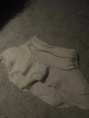 Beige kjol  - Supersnygg beige omlottkjol med volangdetaljer och mjukt, glansigt material. Kjolen har en kort längd och in byggda shorts