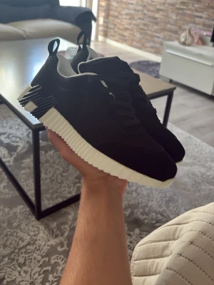 Svarta sneakers med vit sula - Stilrena svarta sneakers med chunky vit sula och coola detaljer på hälen. Ovandelen är i mesh och mockaimitation, med svarta skosnören och dragflikar både fram och bak. Perfekta för dig som gillar en modern och sportig look.