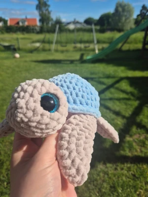 Söt handvirkad Sköldpadda i sammetsgarn 🐢✨ - Otroligt mjuk, handgjord sköldpadda virkad i lyxiga Baby Snuggles (100% polyester). Nygjord i rökfritt hem.🔎 Notering: Finns en minimal, knappt synlig repa på ena plastögat från tillverkningen (se sista bilden). 🧼Tvättråd: Handtvätt/skontvätt i tvättpåse (max 30°), lufttorkas.🧸 Säkerhet: Innehåller säkerhetsögon av plast. Rekommenderas ej till barn under 3 år utan tillsyn.Fraktas spårbart via Plick. 💕