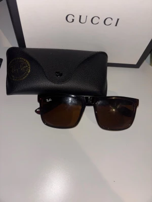 Svarta Ray-Ban solglasögon Wayfarer - Snygga svarta Ray-Ban Wayfarer solglasögon med bruna glas och klassisk fyrkantig form. Kommer med original svart fodral i skinn. Perfekta för dig som vill ha en tidlös och ikonisk look.
