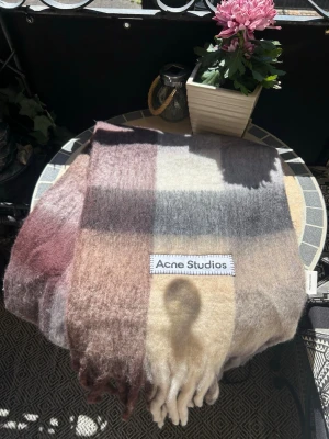 Rutig mohairhalsduk från Acne Studios - Säljer en fluffig och mjuk halsduk från Acne Studios i mohairmix. Halsduken har rutigt mönster i beige, brunt, grått och vinrött. Klassisk Acne Studios-label framtill och fransar i ändarna. Perfekt för dig som vill ha en trendig accessoar med lyxig känsla.