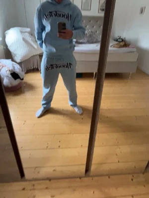 Ljusblå hoodie från 1Locci-It - Säljer en ljusblå hoodie och byxor från hoodrich  och köpta på Jd sports med stor svart logga på bröstet och byxorna. Hoodien har huva och en avslappnad passform, perfekt för en chill och trendig look. Matcha med tillhörande mjukisbyxor för en komplett outfit.