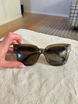 Chimi solglasögon 08 - Snygga solglasögon i olivgrönt transparent plastmaterial med cat eye-form. Bågarna har en cool, bred design och mörka linser. På insidan av skalmen står det 'Designed in Stockholm'. Perfekta för dig som vill sticka ut med en trendig accessoar.Har någon liten repa på glaset men inget som märks