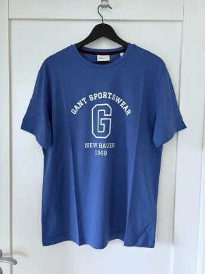 Gant T-shirt, M, Ny! Ord. pris 500kr. - Snygg blå T-shirt från Gant.Rund halsringning och normal passform.  Axelbredd: 47 cm Längd: 72 cm  Mellan armhålorna: 53 cm  Ord. Pris 500kr.  
