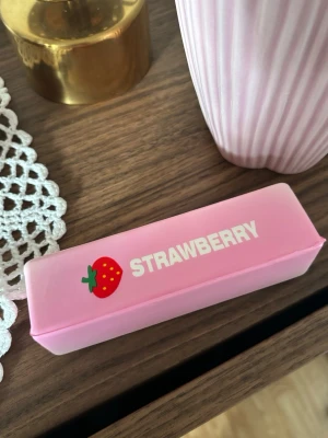Rosa butter squishy leksak med jordgubbstryck - Sött rosa squishy med texten 'STRAWBERRY' och en jordgubbsillustration på locket. Perfekt skick. Slow rising