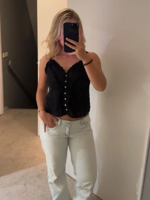 Svart linnetopp med knappar och volang - Säljer ett jättefint svart linne från Zara. Linnet är tunt och luftigt vilket gör det ett super bra plagg i sommar. Linnet har justerbara axelband och är i bra skick.😊😊