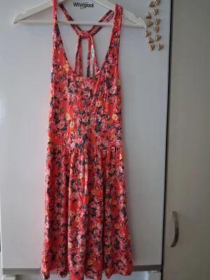 Blommig sommarklänning med knyt - Säljer en färgglad blommig kortklänning i rosa, gul och grön. Klänningen har ärmlös design, rundad halsringning och snygg knytning i ryggen. Perfekt för varma dagar och har ett luftigt, mjukt tyg.