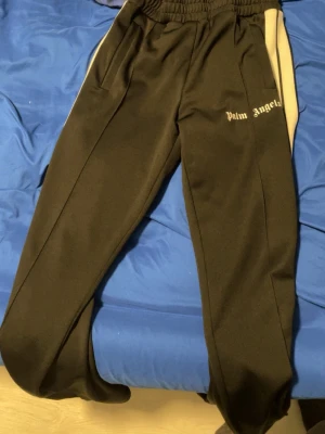 Palm Angels svarta mjukisbyxor M - Svarta mjukisbyxor från Palm Angels med vita sidor och logga på vänster ben. Byxorna har resår i midjan och är gjorda i 100% polyester för en sportig och bekväm känsla. Perfekta för en avslappnad och trendig stil. Använd 1 gång testade det och passade ej mig . Ni får med påse som kom med från Palm angeles