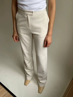 Beige raka kostymbyxor Djerf Avenue - Stilrena beige (greige) kostymbyxor (first choice pants) med hög midja och raka ben. Byxorna har diskreta sidfickor och dold dragkedja framtill. Perfekta för en clean och modern look. Djerf avenue nya med prislapp. Längden tall 