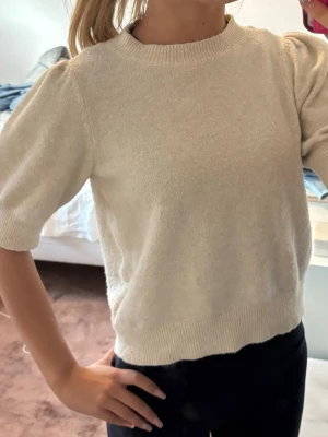 Beige puffärm stickad tröja - Snygg beige stickad tröja med puffärmar och ribbade muddar vid hals, ärmslut och nederkant. Tröjan har en mjuk och lite kortare passform 
