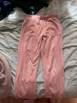 Rosa mjuka byxor med fickor - Säljer ett par mjuka och sköna byxor i rosa velour med bred resår i midjan och stora fickor fram samt bakfickor med knappdetaljer. Perfekta för en chill och avslappnad stil. Materialet är lent och stretchigt för extra komfort.