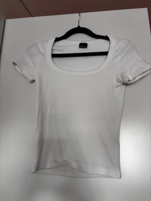 Vit basic t-shirt med rund hals - En klassisk vit ribbad t-shirt med rund, djup ringning och korta ärmar. Den har en ganska lång design. Superskönt material och snygg passform. Använd några gånger. Känner att jag har andra vita t-shirts jag använder mer hemma men den är skitsnygg.