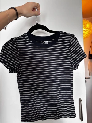 Svartvit randig t-shirt - Skitsnygg mörkblå med vita ränder t-shirt. Tröjan har en figurnära passform och slutar strax vid naveln. Perfekt till jeans eller kjol. Den är verklgien skitnajs passform men  behöver tyvärr rensa! Använd flera gånger men är i superbra skick.