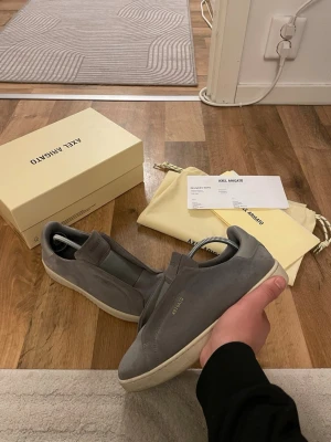 Gråa sneakers från Axel Arigato - Snygga gråa sneakers från Axel Arigato i mocka med minimalistisk design och vit sula. Diskret logga på sidan och klassisk låg modell som passar till det mesta. Skorna har elastiska partier för enkel påtagning och en stilren look.