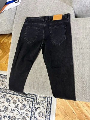 Svarta jeans från AMIRI - Säljer ett par svarta jeans från AMIRI med klassisk femficksdesign och raka ben. Jeansen har en snygg tvättad finish och läderpatch bak i midjan. Perfekta för dig som gillar streetwear och vill ha en stilren look.
