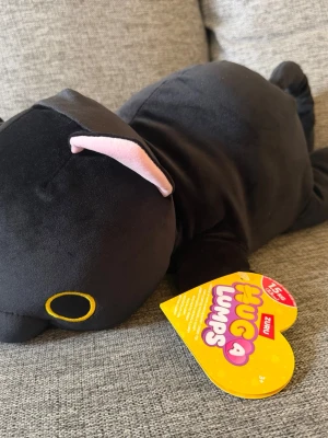 NY! Zuru Hug A Lumps Katt Luna 1,5kg! - Supermjuk svart gosedjurskatt från Hug a Lumps med söta rosa öron och broderade gula ögon. Perfekt att krama och ha som sällskap i soffan eller sängen. Tillverkad i plyschmaterial och har en rund, gosig form. Ny i kartong!