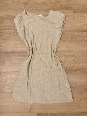 Klänning från H&M basic 146/152 - En enkel och mjuk ljusgrå klänning från H&M Basic. Klänningen har rund halsringning, ärmlös design och är tillverkad i bomull. Perfekt för en avslappnad och bekväm stil. Storlek 146/152 och defekter förekommer (se bilder)