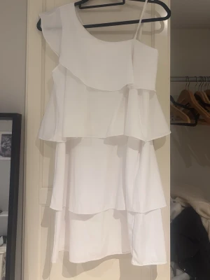 Vit volang klänning 💕 - Otroligt söt vit klänning från Gina Tricot i storlek 164. Modellen är asymmetrisk (one shoulder) med ett smalt axelband på ena sidan och superfina volanger i flera lager som ger ett fantastiskt fint fall. Perfekt till skolavslutning, sommarfester eller midsommar!