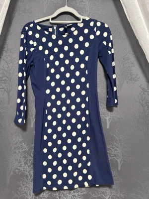 Mörkblå prickig klänning H&M Divided - Mörkblå kortklänning från H&M Divided med vita prickar och trekvartsärm. Klänningen har en figurnära passform och är tillverkad i mjuk bomullsmix. Perfekt för dig som gillar retrovibbar och lekfull stil.