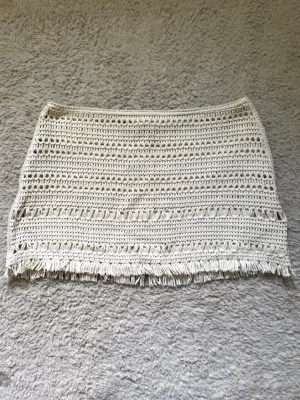 Beige mini kjol  H&M - Säljer en beige kjol från H&M med snygga virkade detaljer och fransar längs nederkanten. Kjolen har ett fodrat innerlager!