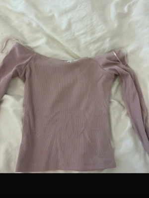 Ljuslila ribbad offshoulder topp - Säljer en ljuslila ribbad offshoulder topp från Pull&Bear. Toppen har lång ärm och är tillverkad i mjuk, stretchig bomullsmix. Perfekt för dig som gillar en enkel men trendig stil.