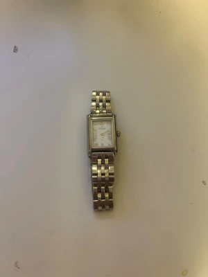 Klassisk silverfärgad armbandsklocka från Mockberg - Stilren armbandsklocka i silver med rektangulärt ur och länkarmband ifrån mockberg. Urtavlan är vit med romerska siffror och tunna visare. Perfekt accessoar för dig som gillar en tidlös och elegant look.