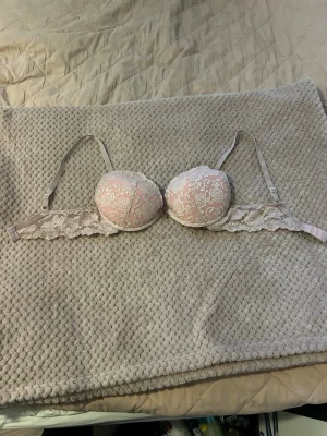 Rosa push-up bh med spetsdetaljer - Säljer en snygg push-up bh i ljusrosa med vita spetsdetaljer. Bh:n har vadderade kupor och justerbara axelband. Spetsen går längs hela bandet och ger en romantisk känsla. Perfekt för dig som gillar feminina underkläder.