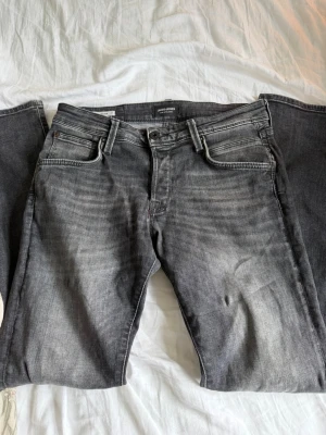 Jack & Jones jeans - Säljer ett par grå slim fit jeans med klassisk femficksmodell och snygga slitningar. Jeansen har normal midja och raka ben. Perfekta till en avslappnad stil och passar till det mesta i garderoben.