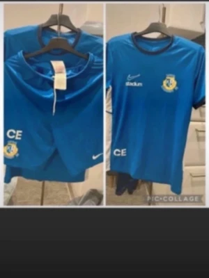 Blå Nike träningsset med klubbmärke - Säljer ett blått träningsset från Nike med klubbmärke och initialerna CE. Setet består av en t-shirt och ett par shorts, båda i 100% polyester. T-shirten har rund hals och tryckta loggor från Nike och Stadium. Perfekt för träning eller match.