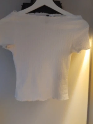 Vit ribbad topp från H&M - Säljer en söt vit ribbad topp från H&M i storlek XXS. Toppen har korta ärmar, offshoulder-modell och stretchigt material som sitter tight. Perfekt att matcha med jeans eller kjol för en trendig look.