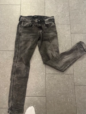 Gråa replay anbass jeans storlek 31-34 - Säljer ett par grå replay anbass jeans i storleken 31 34 med klassisk femficksdesign och svarta detaljer. Jeansen har en tvättad look och smala ben som sitter snyggt. Perfekta för dig som gillar en avslappnad men trendig stil. Hör av er vid frågor eller funderingar!!