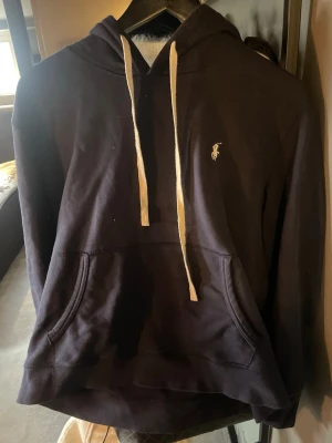 Mörkblå hoodie från Polo Ralph Lauren - Mörkblå hoodie från Polo Ralph Lauren med vit broderad logga på bröstet och vita dragsnören i huvan.  Skicket är väldigt bra och stilren.