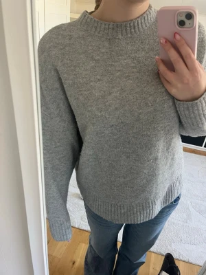 Grå stickad tröja  - Mysig grå stickad tröja med rund hals och ribbade muddar vid ärmslut och nederkant. Tröjan har en avslappnad passform och är perfekt för kyliga dagar. Materialet känns mjukt och värmande. Enkel och stilren design som passar till det mesta.