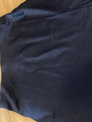 Mörkblå kjol från Kappahl - Snygg mörkblå långkjol från Kappahl i glansigt satinliknande material. Kjolen har en enkel och stilren design som ger en elegant look. Perfekt att matcha med en crop top eller stickad tröja för en trendig outfit.🤪