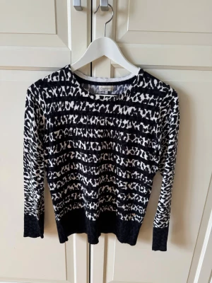 Svartvit leopardmönstrad stickad tröja - Snygg stickad tröja från Cappuccini i svartvitt leopardmönster. Tröjan har rund halsringning, långa ärmar och ribbade muddar vid ärmslut och nederkant. 