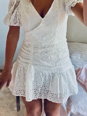 Vit omlottklänning med puffärm. Missguided.S - Supersöt vit kortklänning med omlott och v-ringning, puffärmar och volangkant. Klänningen har broderade spetsdetaljer och snörning i midjan för en snygg passform. Perfekt för sommarens alla tillfällen!