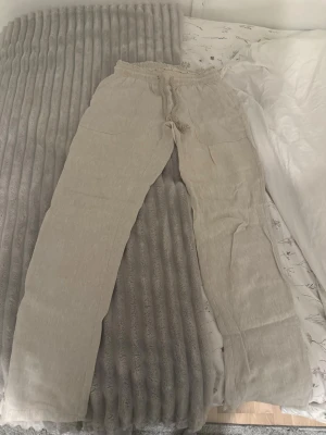 Beiga linnebyxor  - Säljer ett par beiga linnebyxor med avslappnad passform och resår i midjan samt dragsko. Byxorna har raka ben och två fickor framtill. Perfekta för en chill och stilren look. Köpta för 800kr. Knappt använda.