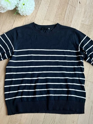Marinblå randig stickad tröja 157 - Snygg marinblå stickad tröja från 157 med vita horisontella ränder. Tröjan har rund halsringning, ribbade muddar och en klassisk, avslappnad passform. Perfekt för en stilren och enkel look.